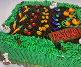 Sheet cake decorated as a garden with buttercream grass, dirt made of cake crumbs, rows of vegetables like carrots, tomatoes, and pumpkins, and small chicken figures.