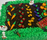 Sheet cake decorated as a garden with buttercream grass, dirt made of cake crumbs, rows of vegetables like carrots, tomatoes, and pumpkins, and small chicken figures.