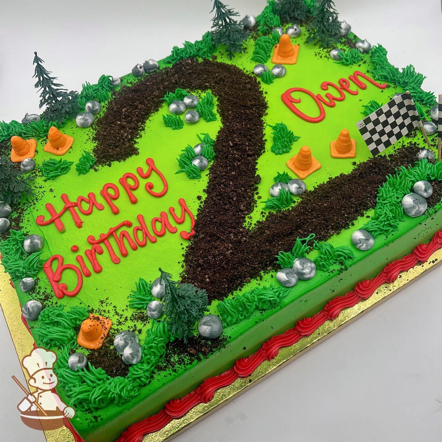 Sheet cake with green frosting, a dirt track in the shape of the number 2 made of cake crumbles, plastic trees, orange construction cones, silver rocks, and a checkered flag.
