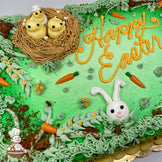 Sheet cake with green frosting, a buttercream nest holding three yellow chicks, a white bunny face, orange chocolate carrots, and cake crumb "dirt."