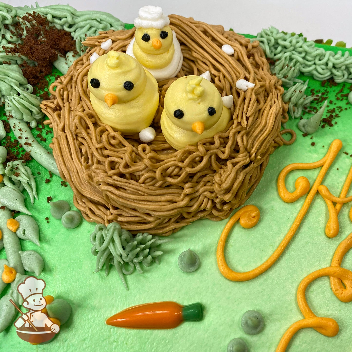 Sheet cake with green frosting, a buttercream nest holding three yellow chicks, a white bunny face, orange chocolate carrots, and cake crumb "dirt."
