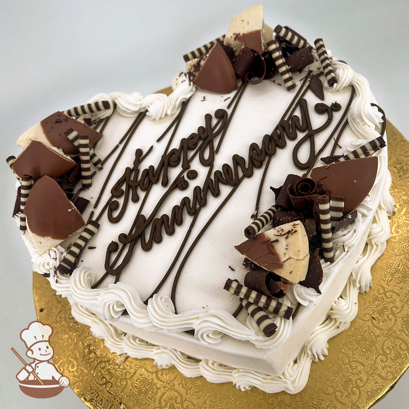 Heart-shaped cake with white frosting, chocolate ganache stripes, and Belgian chocolate decorations, including curls and dipped shortbread pieces.