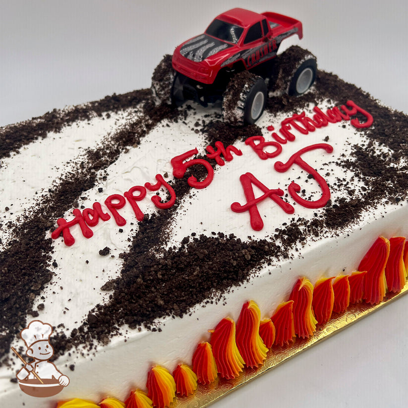 Sheet cake with white frosting, a red toy monster truck toy on top, crushed cake "dirt" tracks, and red and yellow flame decorations on the sides.