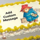 Illustration of a bear in a red hat and blue coat holding a suitcase labeled "Wanted on Voyage" and a jar, with a white background. Printed on a sheet cake.