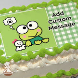 A cartoon frog with large eyes and pink cheeks sits next to a small ghost-like figure with a pink bow. The background is green with a gingham pattern. Printed on a sheet cake.