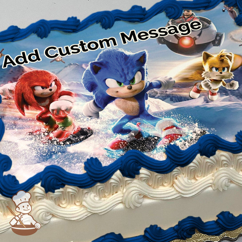 Sonic, Knuckles, and Tails are depicted in a snowy action scene, with Sonic and Knuckles snowboarding and Tails flying. A snowy mountain background is visible. Printed on a sheet cake.