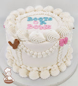 White single-tier cake with piped swirls, pearl accents, and text reading "Boots or Bows" in blue and pink. Decorated with a brown boot and pink bow.