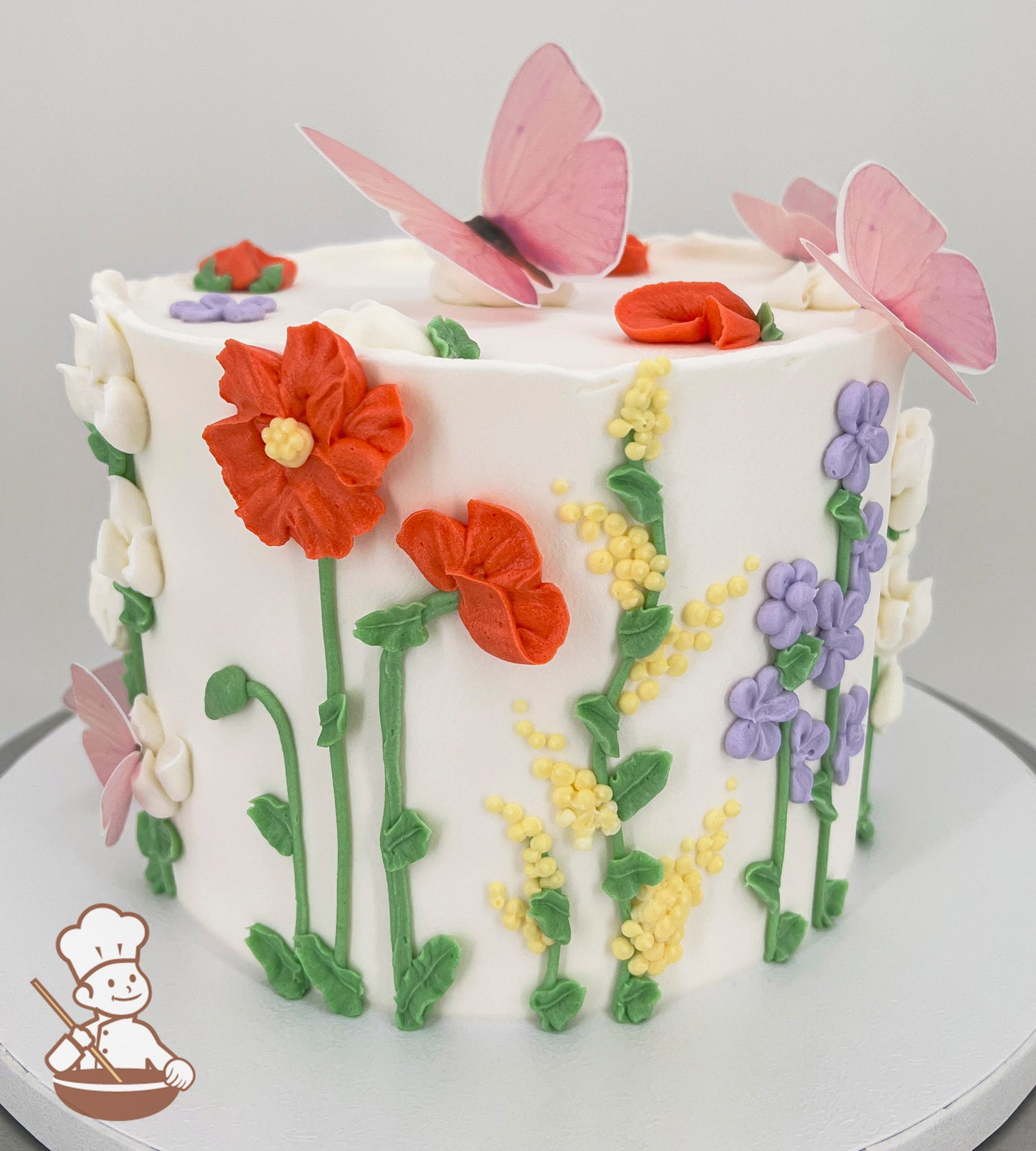 A single-tier white cake decorated with colorful buttercream flowers, including red, yellow, purple, and white blooms, and green stems. Pink butterflies adorn the top.