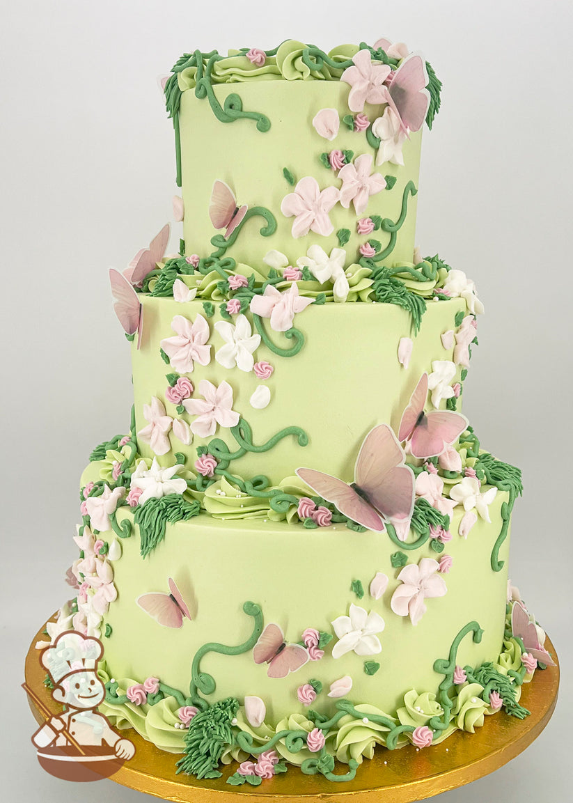 Three-tiered cake with light green frosting, adorned with pink and white buttercream flowers, green vines, and delicate pink butterfly decorations on a gold base.