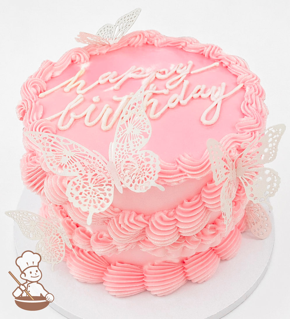 A single-tier pink cake with piped frosting borders, "happy birthday" written on top, and decorated with delicate white butterfly toppers.