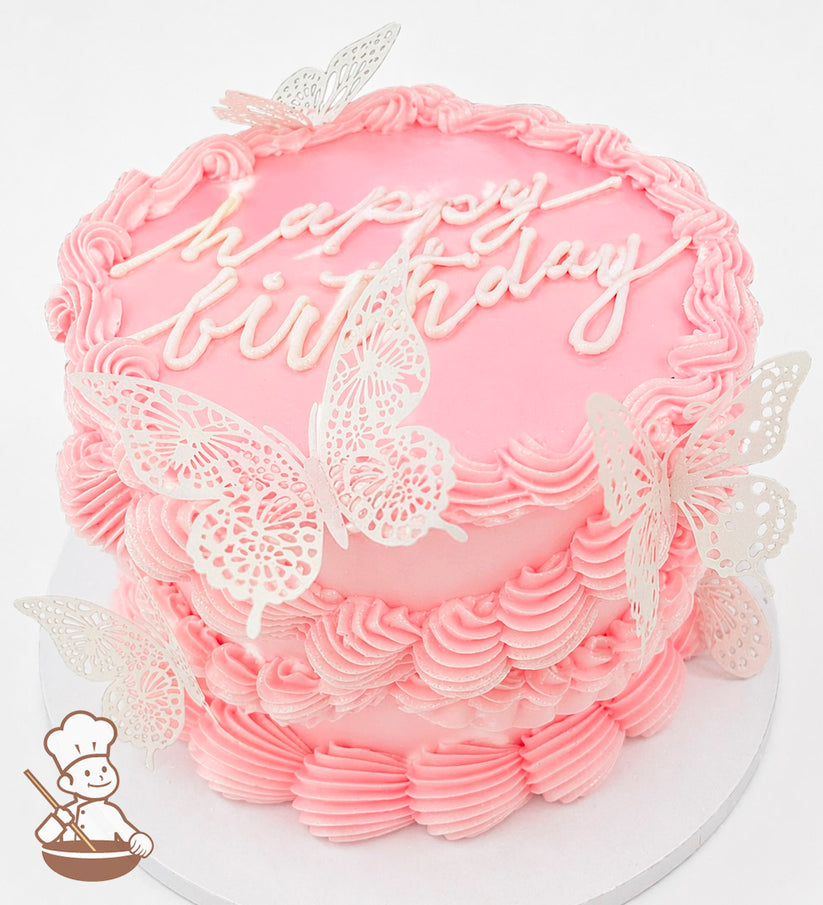 A single-tier pink cake with piped frosting borders, "happy birthday" written on top, and decorated with delicate white butterfly toppers.