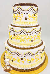 Three-tier white cake with yellow floral and brown dot designs, adorned with piped yellow and white frosting ruffles and brown accents on a gold base.