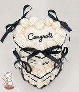 A two-tiered heart-shaped cake with white frosting, black piped accents, and black ribbon bows. The top tier features the word "Congrats" in black script.