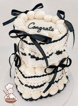 Two-tiered white cake with piped frosting details, black ribbon accents, and the word "Congrats" written on top in black.