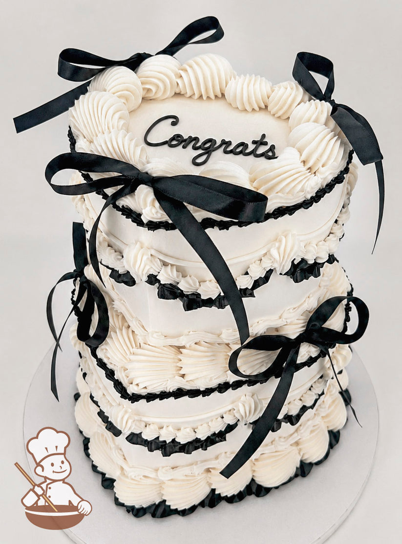 Two-tiered white cake with piped frosting details, black ribbon accents, and the word "Congrats" written on top in black.
