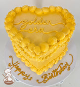 A heart-shaped, single-tiered golden cake with shell-like frosting details. "Golden Era" is written on top, and "Happy Birthday" decorates the base.