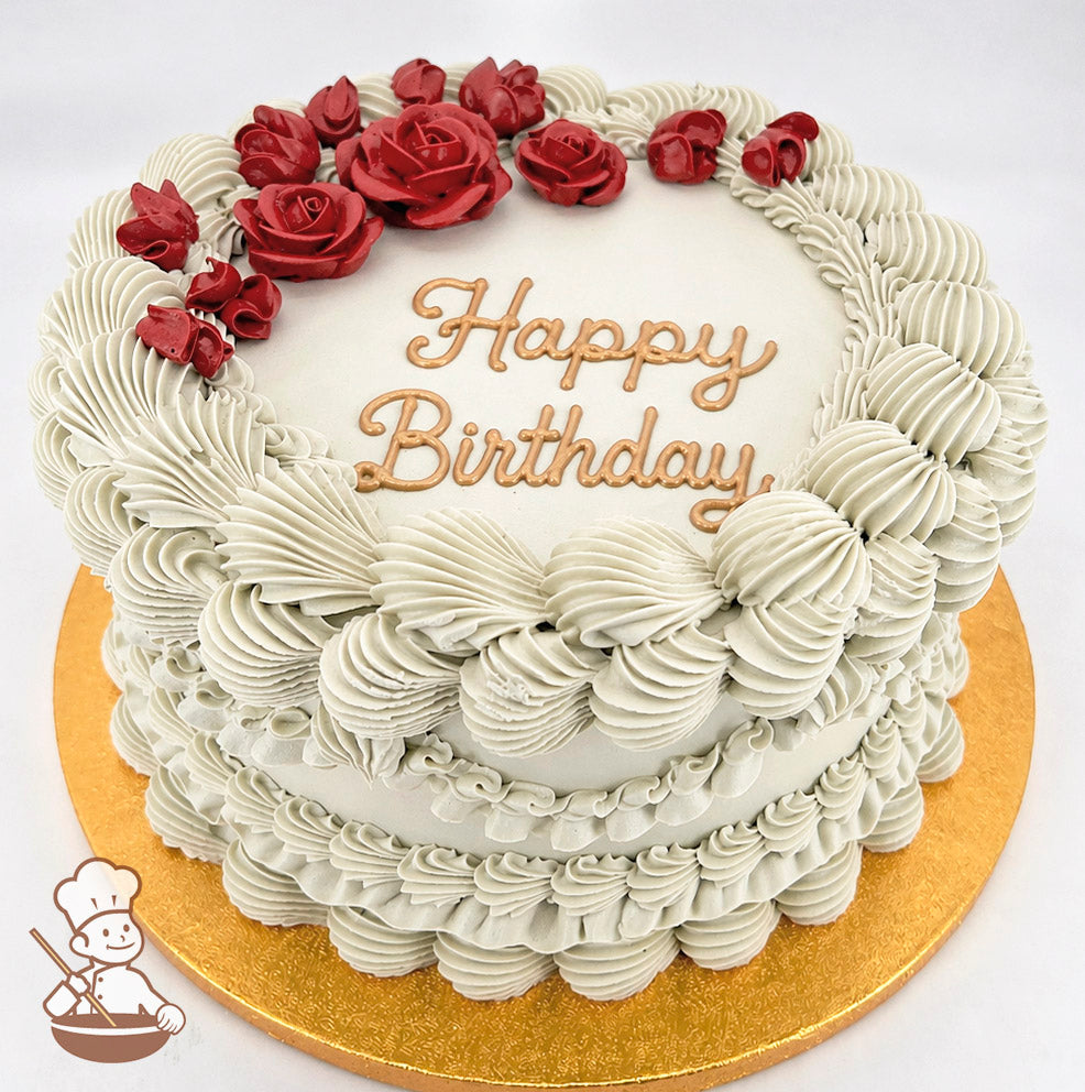A single-tier round cake with beige frosting, intricate piped details, red buttercream roses, and "Happy Birthday" written in gold on top. It sits on a gold board.
