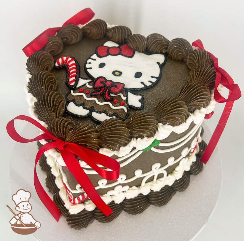 Heart-shaped brown cake with piped brown and white frosting, featuring a Hello Kitty design on top. Decorated with red satin bows and candy cane accents.
