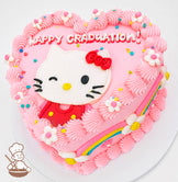 Heart-shaped pink cake with "Happy Graduation!" text, featuring a winking Hello Kitty design, piped pink frosting, rainbow accents, and small flower decorations.