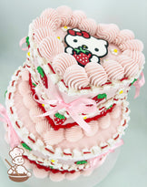 A two-tier heart and round shaped cake with pink frosting, piped swirls, strawberry decorations, and a Hello Kitty topper holding a strawberry. Pink ribbons accent the design.