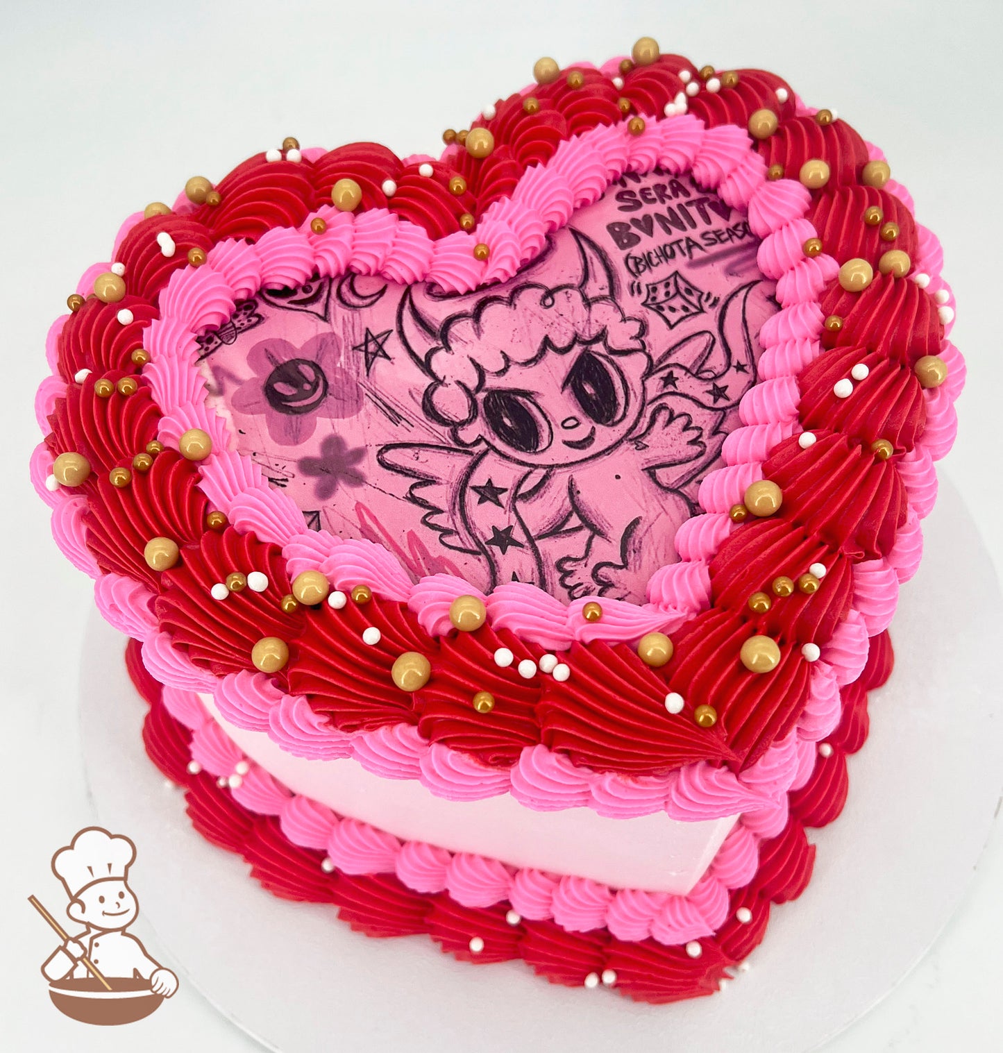 Heart-shaped cake with pink and red piped frosting, adorned with gold and white sprinkles. The top features a cartoon-style illustration of a winged character.