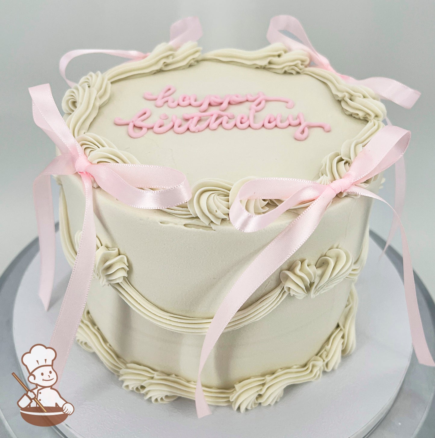 A single-tier off white cake with piped cream borders, pink ribbon bows, and "happy birthday" written in pink icing on top.