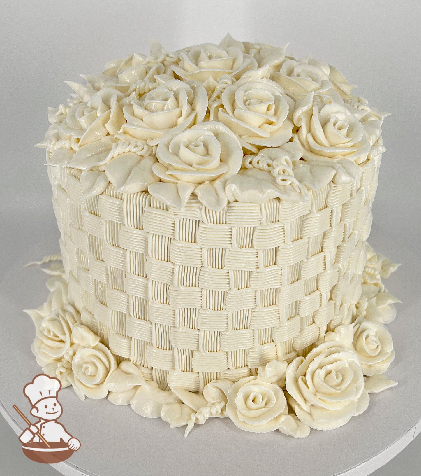 A single-tier cake with intricate white buttercream basketweave piping, topped and surrounded by detailed buttercream roses and leaves.