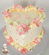Heart-shaped cake with pastel cream frosting, adorned with pink and white silk flowers, piped cream swirls, pearl accents, and the number "23" in pink icing on top.
