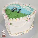 Heart-shaped cake with white frosting, pastel piping, and floral accents. The top features Snoopy and Woodstock on a grassy field with a blue sky and clouds.