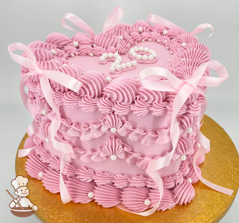 A pink, single-tiered cake with intricate piped frosting, pearl accents, and pink ribbon bows. The top tier features the number "20" in pearls.