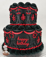 A two-tier black buttercream cake with ornate red piping details, including floral patterns and draped designs. The bottom tier features "happy birthday" written in red.