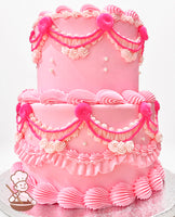 Two-tier pink cake with intricate piping details, including ruffles, swirls, and pearl accents. Decorated with bright pink draped icing and rosettes.