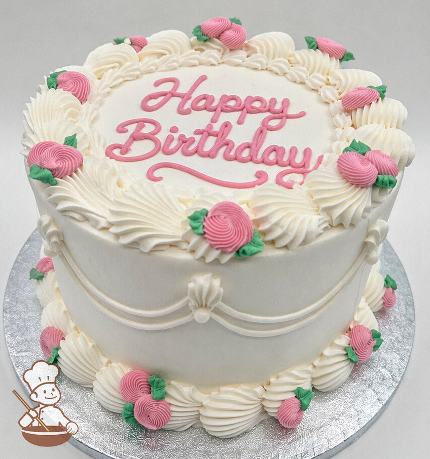 Round cake with white frosting, pink "Happy Birthday" text, and pink rosette decorations with green leaves. Placed on a silver board.