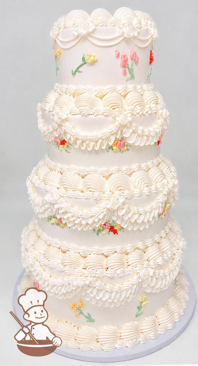 Four-tier white cake with intricate piped frosting swirls and scalloped designs. Decorated with small pastel-colored floral accents on each tier.