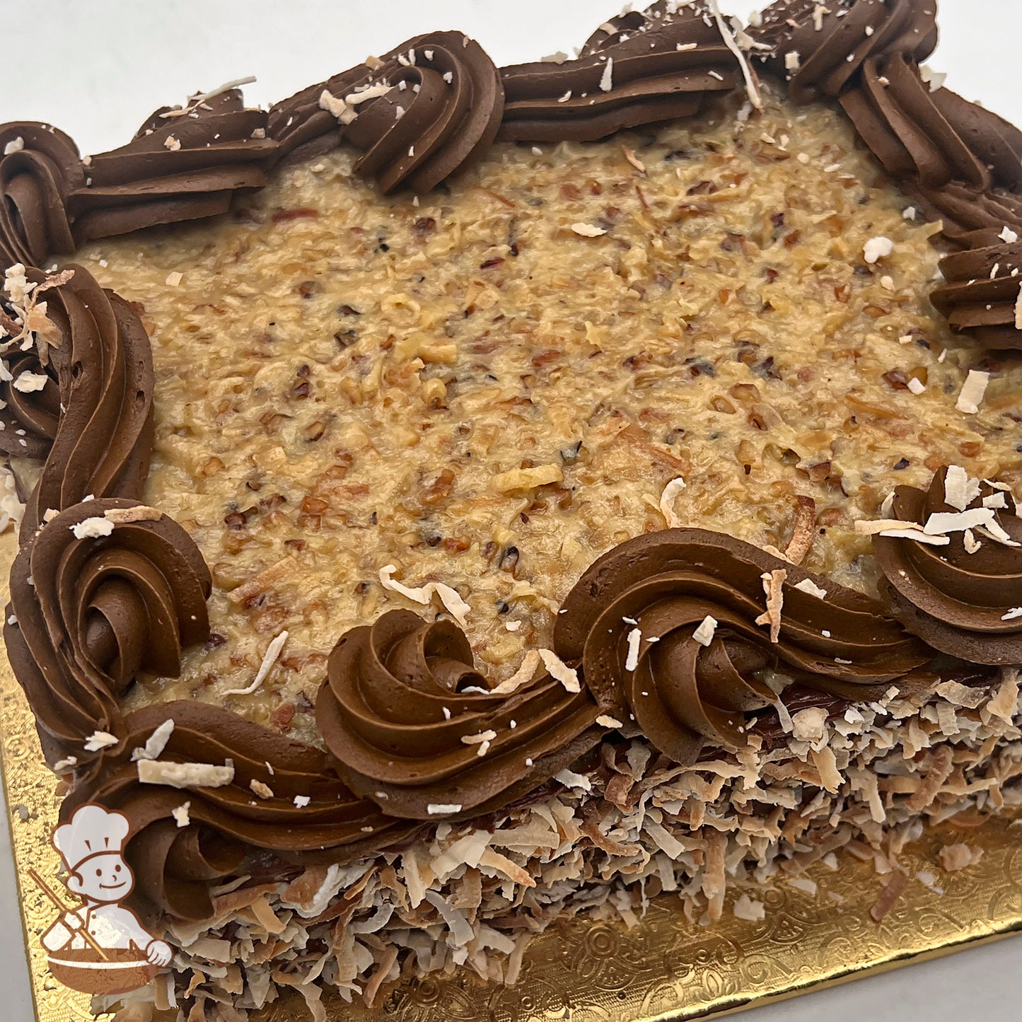 Rectangular sheet cake with chocolate buttercream icing swirls, topped with toasted coconut and walnuts.