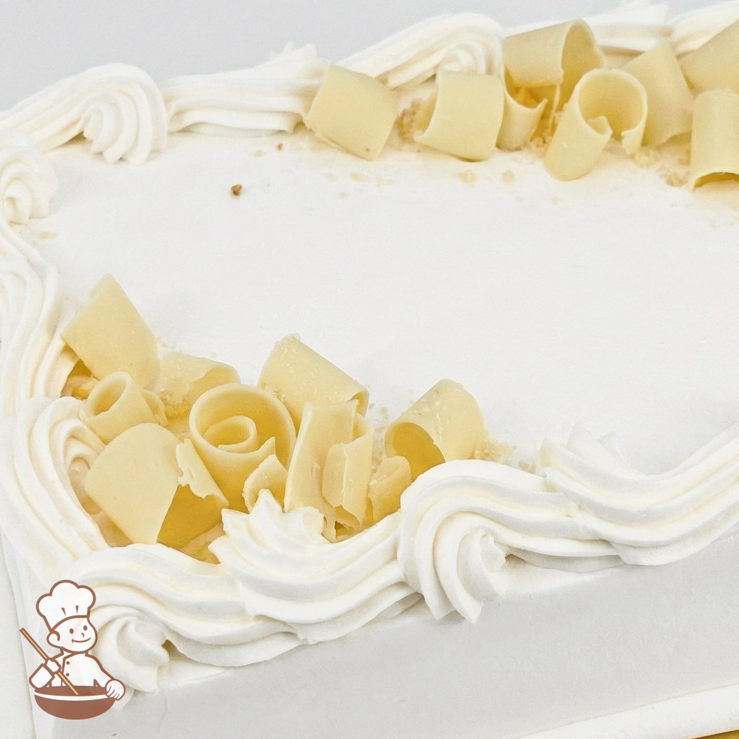White sheet cake with buttercream swirled trim and topped with white chocolate curls.
