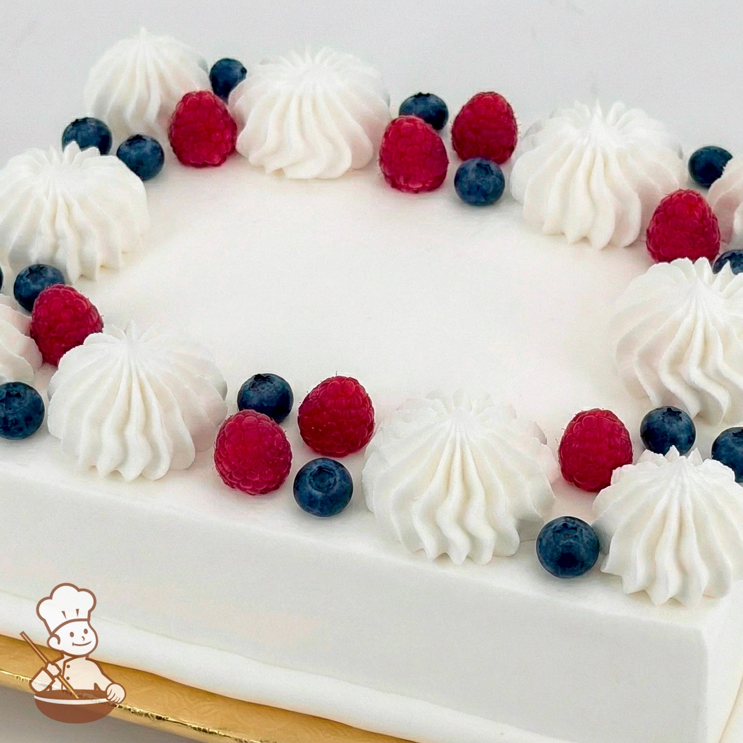 White sheet cake topped with buttercream swirls, blueberries, and raspberries.