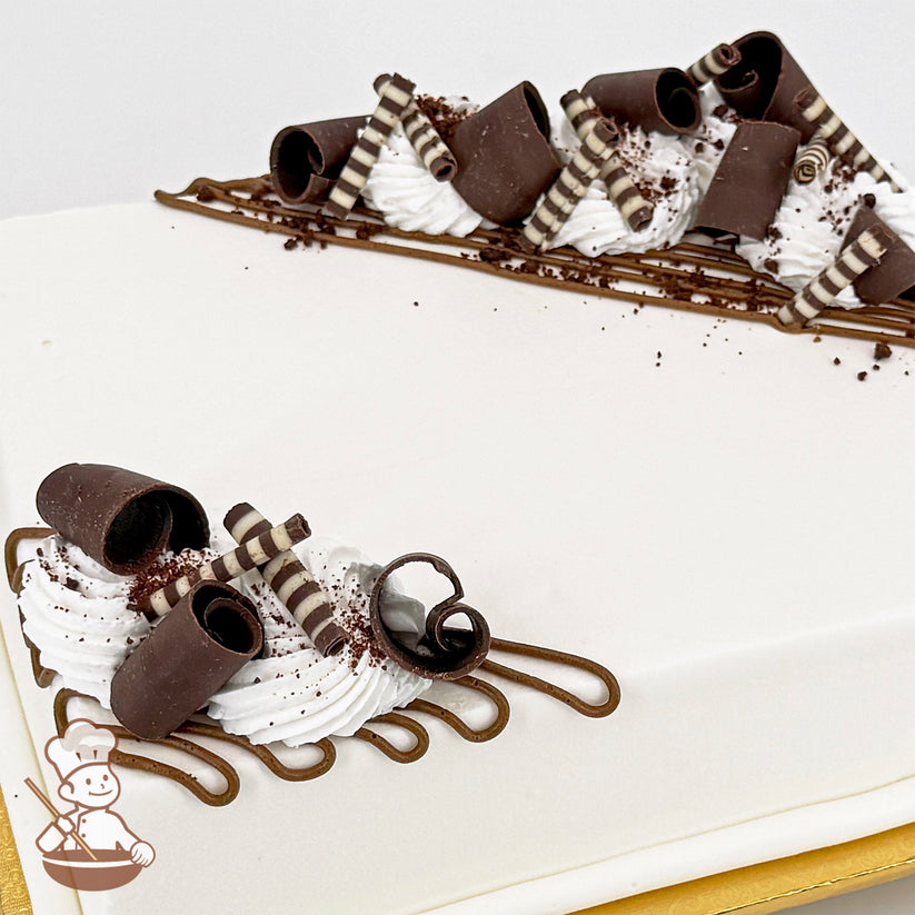 White sheet cake decorated with chocolate curls, striped chocolate sticks, brown buttercream lines, and white buttercream swirls.