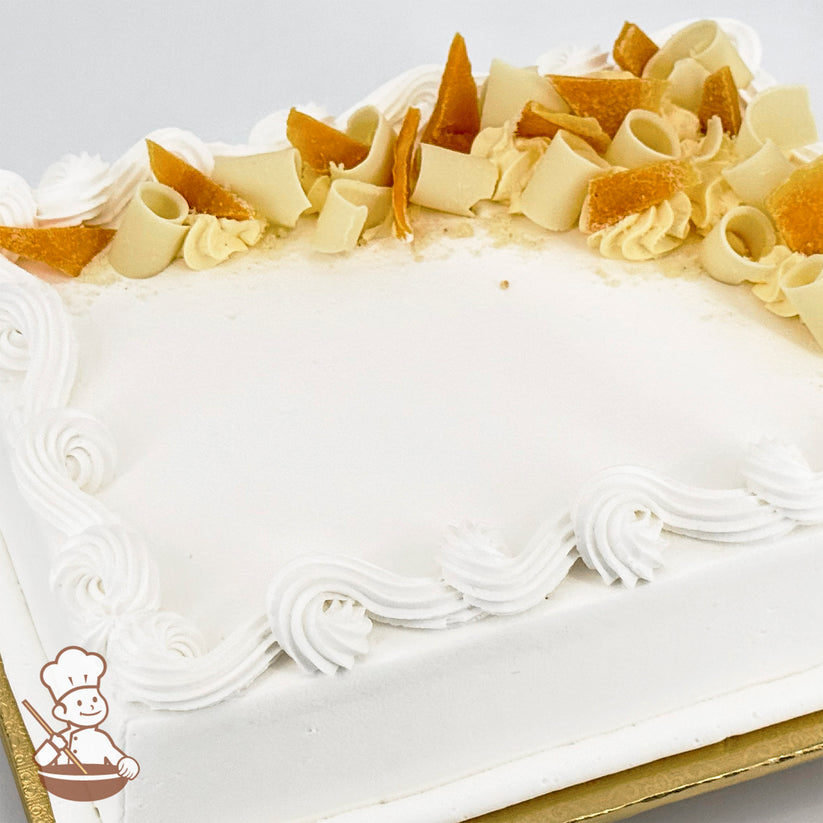 White sheet cake with swirled trim topped with white chocolate curls and dried mango peels.