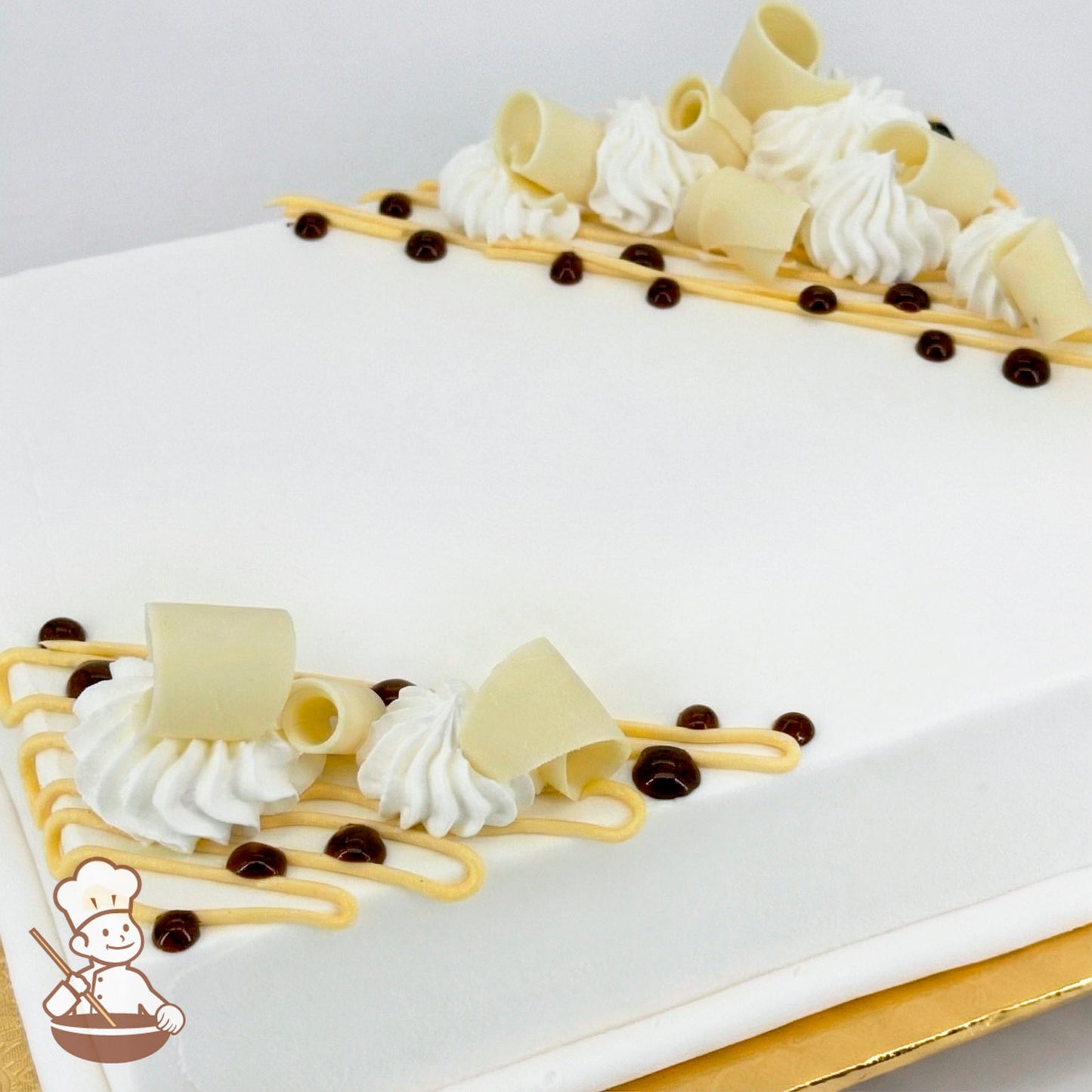 White sheet cake with white chocolate curls, white buttercream swirls, yellow buttercream lines, and small chocolate dots.