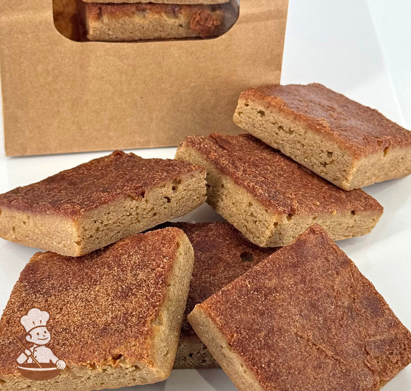 Six snickerdoodle blondies with a golden-brown top and moist, soft texture are displayed in front of a kraft window bag.