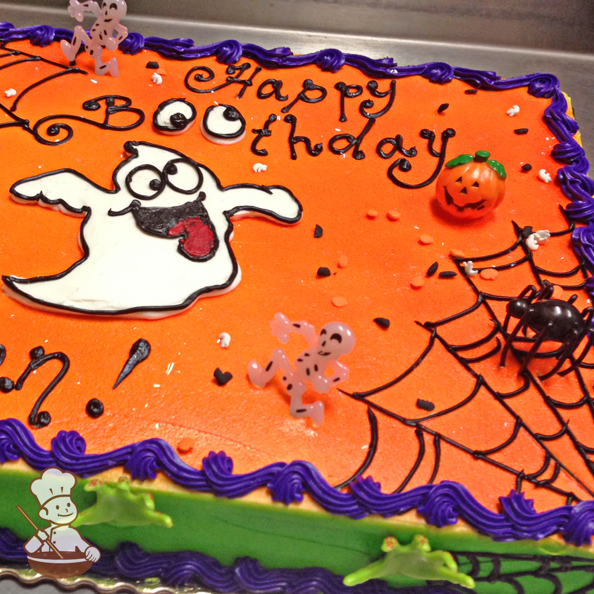 Birthday sheet cake with buttercream piped ghost with silly eyes and piped spider webs and pumpkin and spider toy rings.