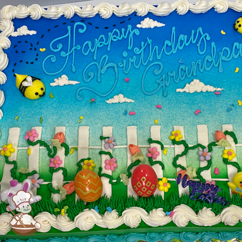 Birthday sheet cake with buttercream fence covered in flower vines and flying bumble bee and easter egg and bunny toy.
