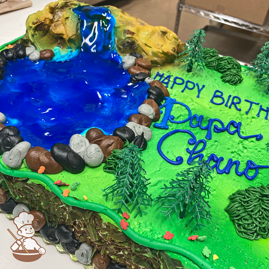 Birthday sheet cake with buttercream piped rocks forming a water pond with waterfall inside a park field.