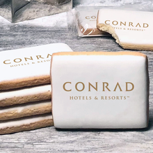 Load image into Gallery viewer, A stack of rectangle butter shortbread cookies with Conrad Hotels and Resorts logo printed directly on a white, lemon sugar icing.