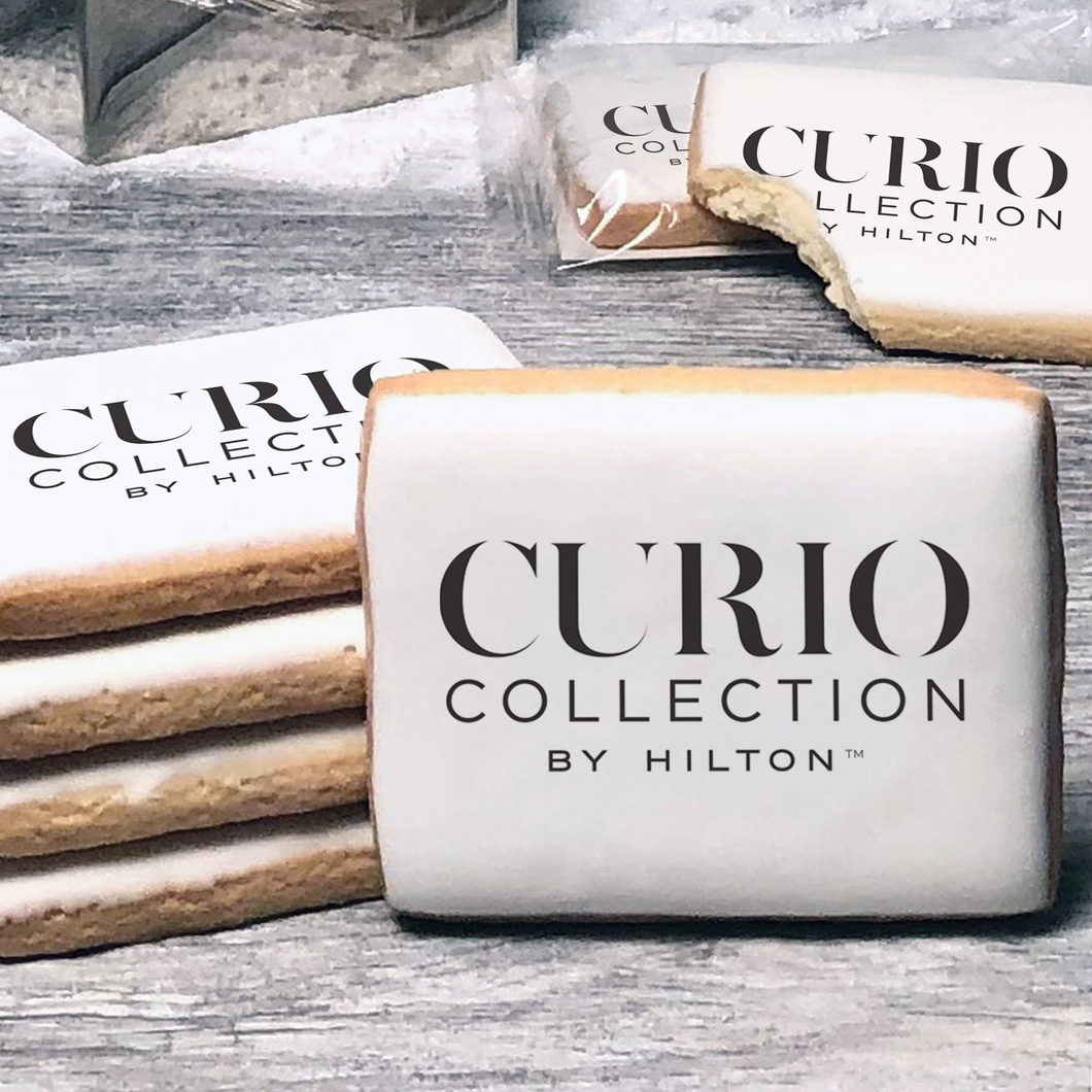 A stack of rectangle butter shortbread cookies with Curio Collection by Hilton logo printed directly on a white, lemon sugar icing.