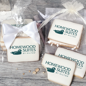 A stack of rectangular butter shortbread cookies with Homewood Suites by Hilton logo printed directly on a white, light sugar icing. Some cookies are shown in clear packaging with a twist-tie ribbon bow or inside an organza bag.