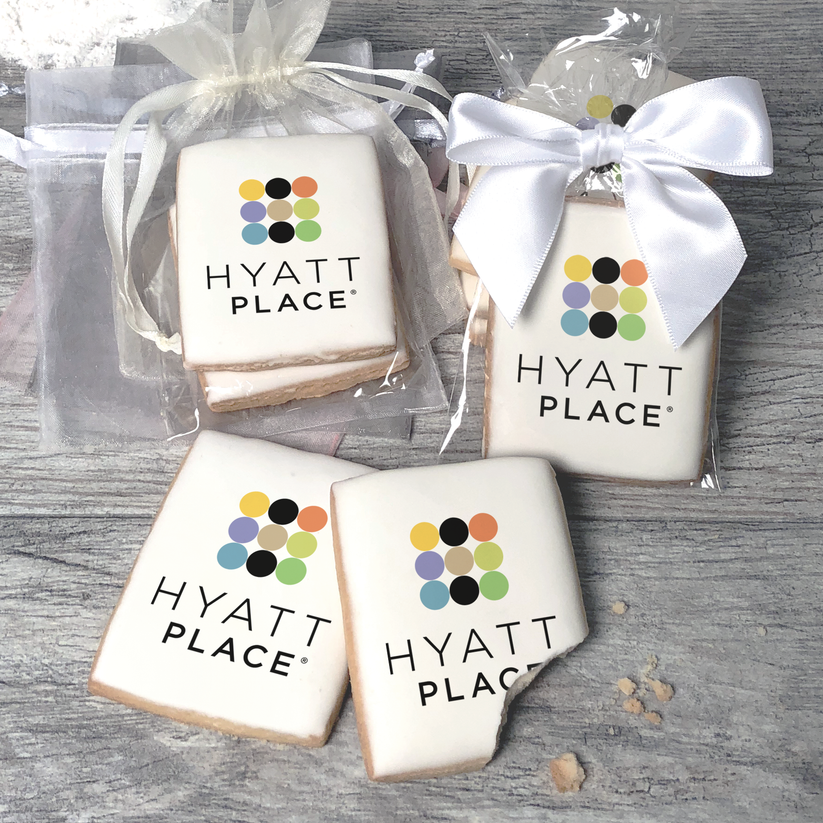 A stack of rectangular butter shortbread cookies with Hyatt Place logo printed directly on a white, light sugar icing. Some cookies are shown in clear packaging with a twist-tie ribbon bow or inside an organza bag.