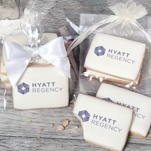 Load image into Gallery viewer, A stack of rectangular butter shortbread cookies with Hyatt Regency logo printed directly on a white, light sugar icing. Some cookies are shown in clear packaging with a twist-tie ribbon bow or inside an organza bag.