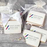 A stack of rectangular butter shortbread cookies with Hyatt Zilara logo printed directly on a white, light sugar icing. Some cookies are shown in clear packaging with a twist-tie ribbon bow or inside an organza bag.